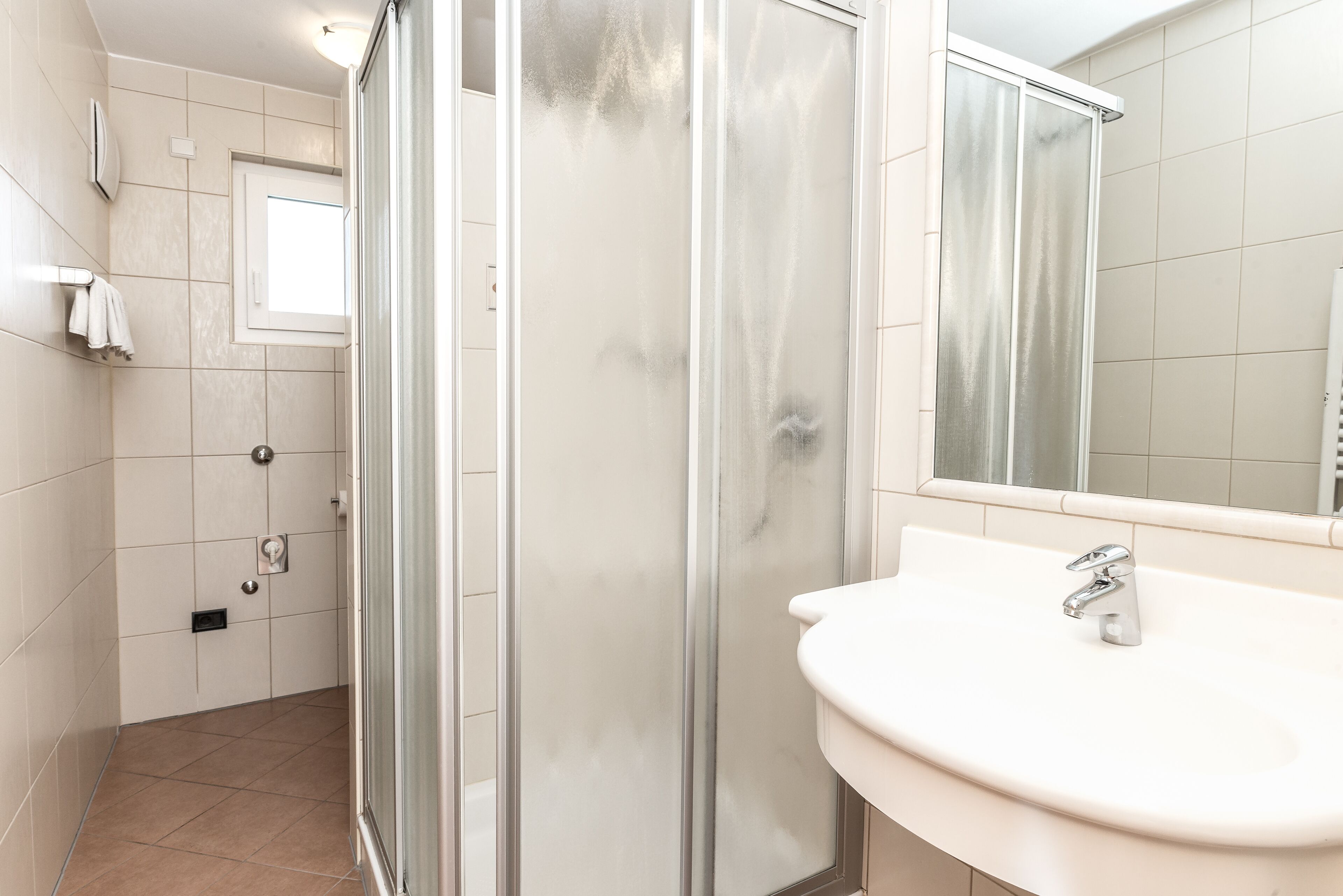 A bathroom with a glass-enclosed shower, a white sink, and a mirror above it.