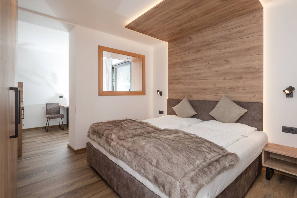 A modern bedroom with a wooden headboard, a large mirror, and a fur throw on the bed.