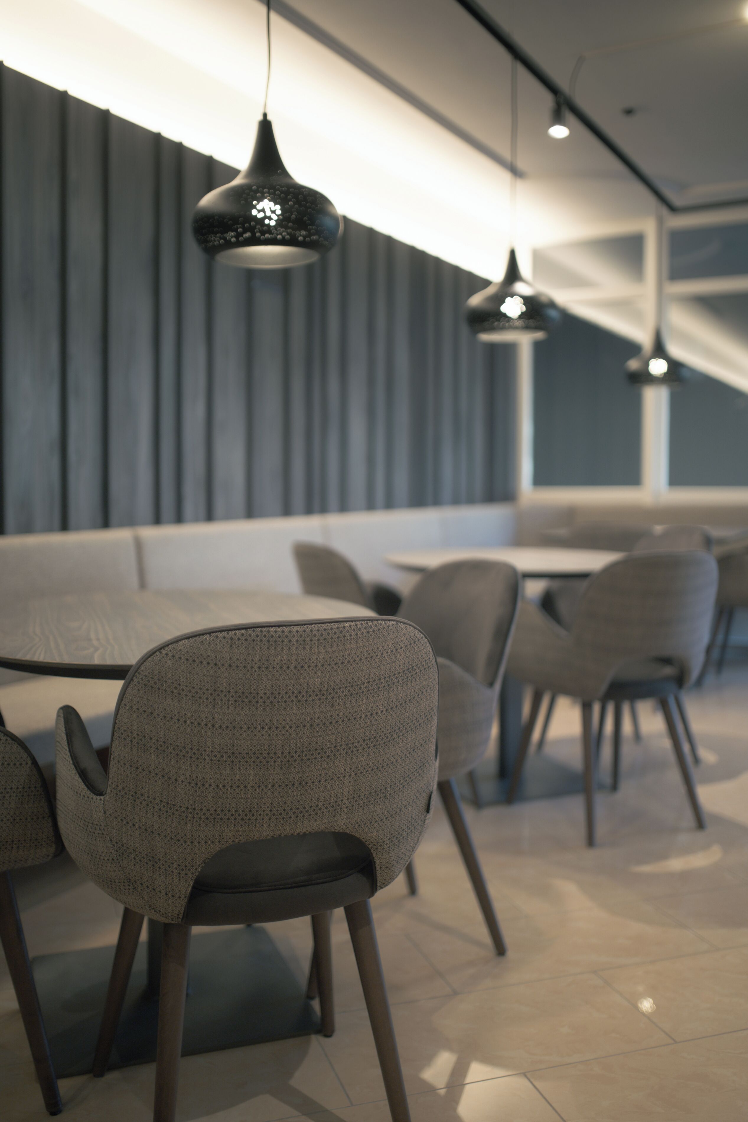 Ein modernes Restaurant-Interieur mit einem langen Esstisch, grauen gepolsterten Stühlen und Pendelleuchten.