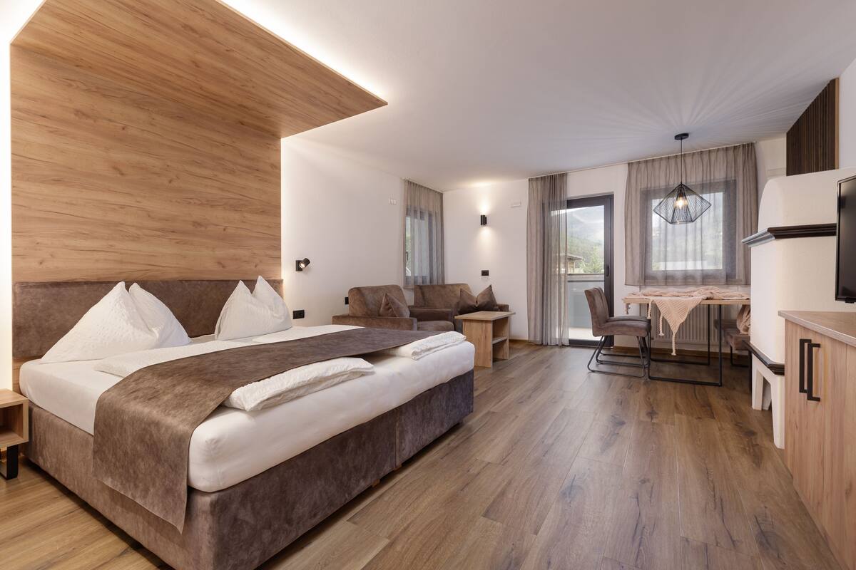 A modern hotel room with a large bed, a desk, and a kitchenette.