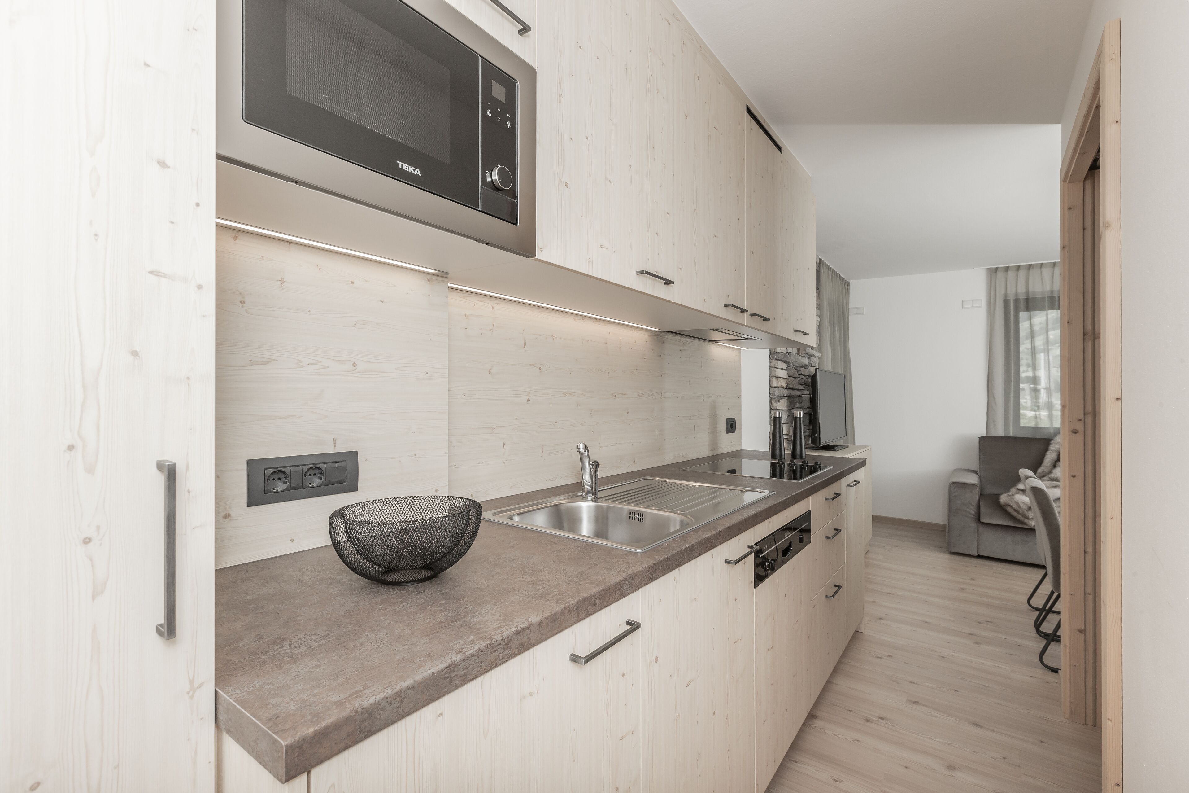 Eine moderne Küche mit Holzausstattung, einer Edelstahlspüle und einer eingebauten Mikrowelle.