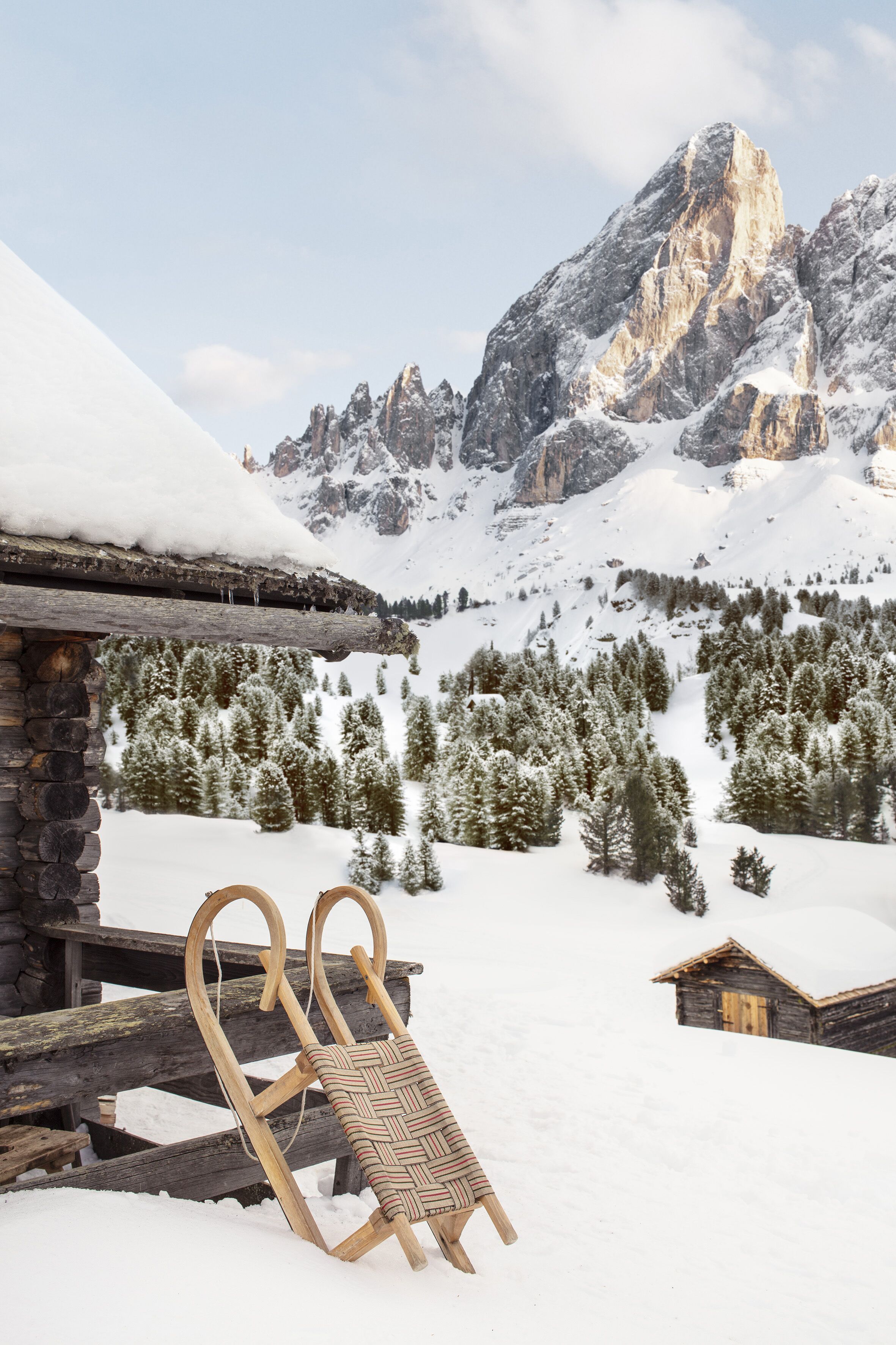 Un trineo de madera apoyado en una cabaña, con una montaña nevada al fondo.