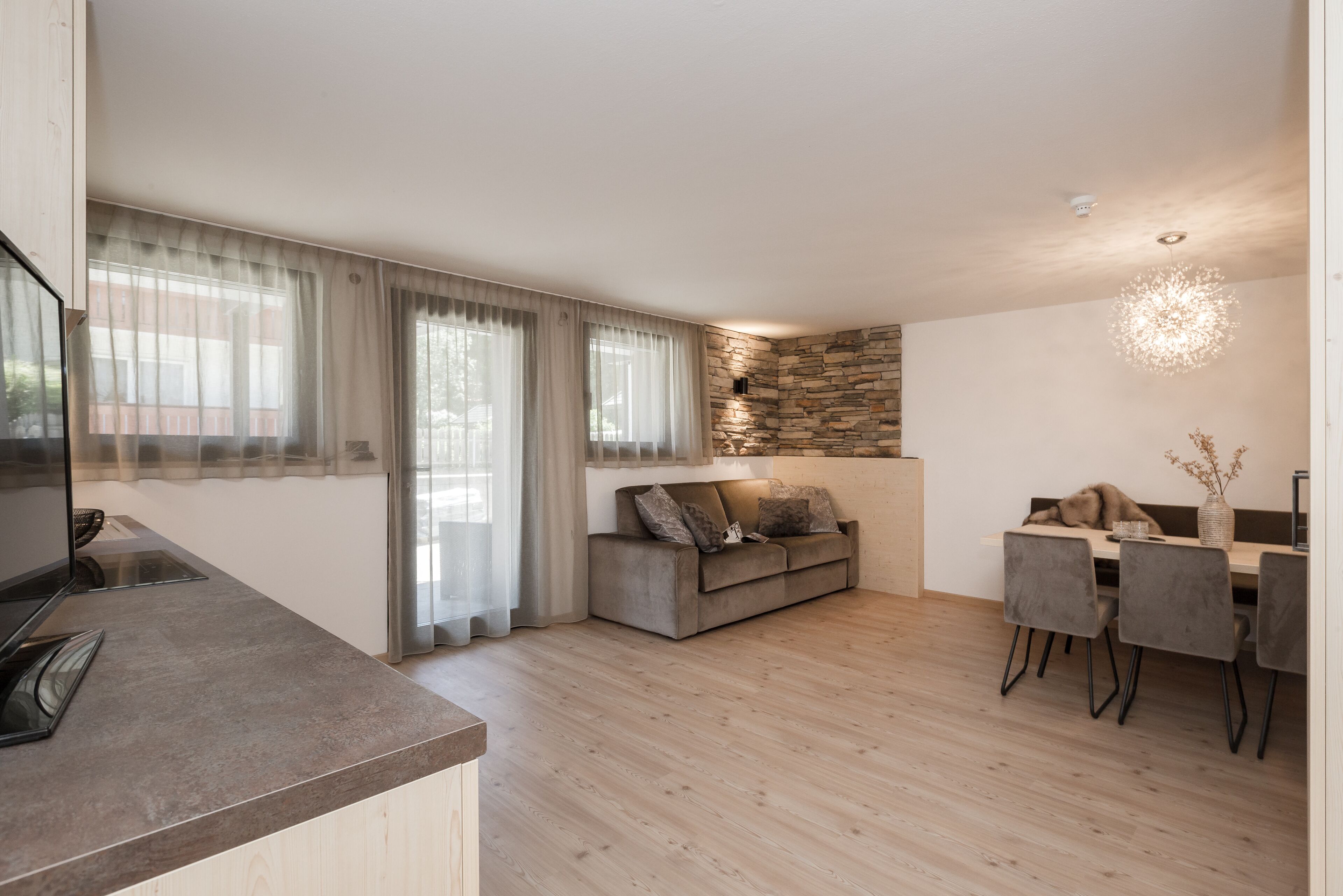 A modern living space with a kitchen area, a dining table with chairs, a sofa, and a stone accent wall.