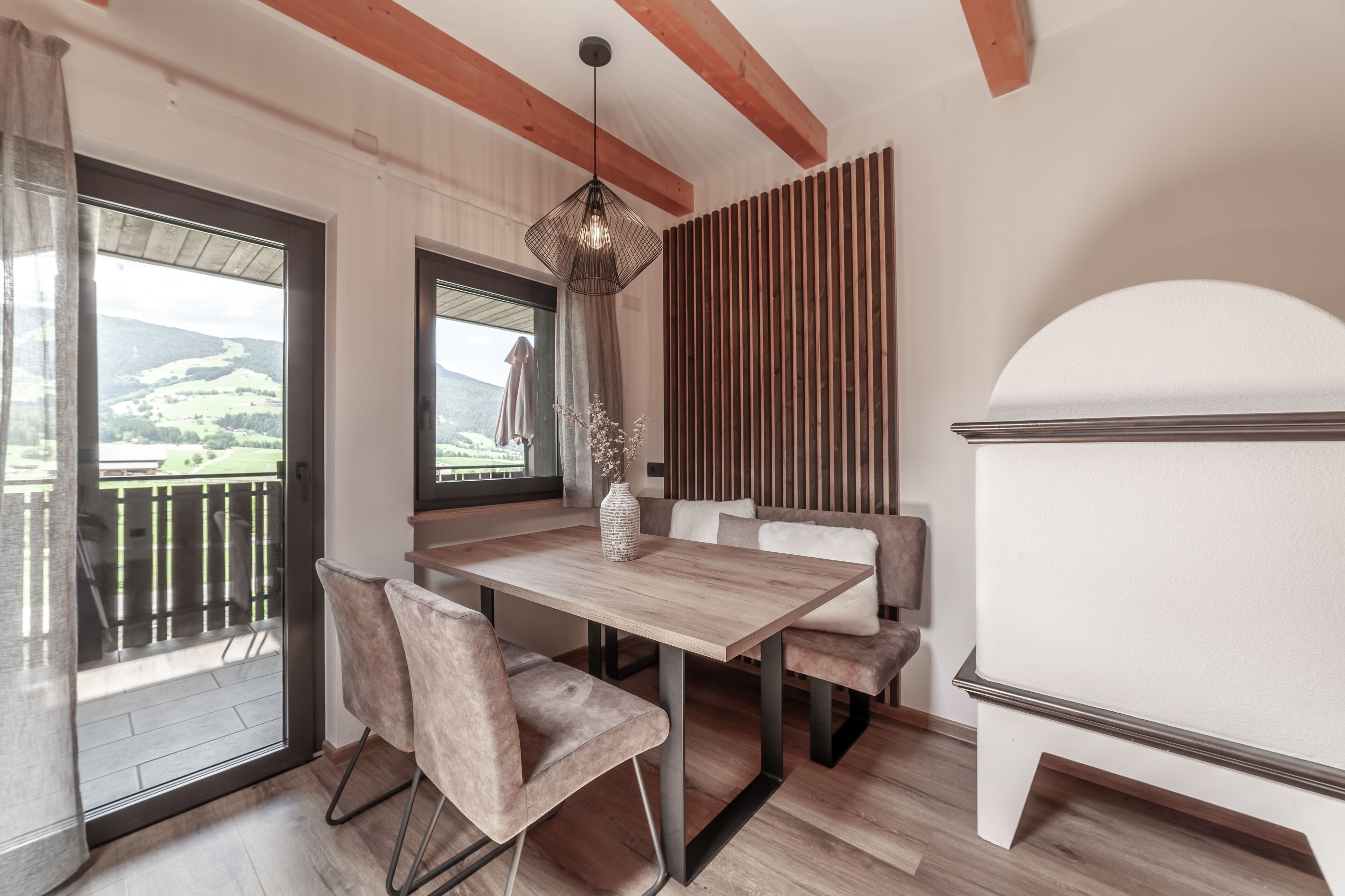 Zona pranzo con tavolo e sedie in legno, lampadario e vista sull'esterno.