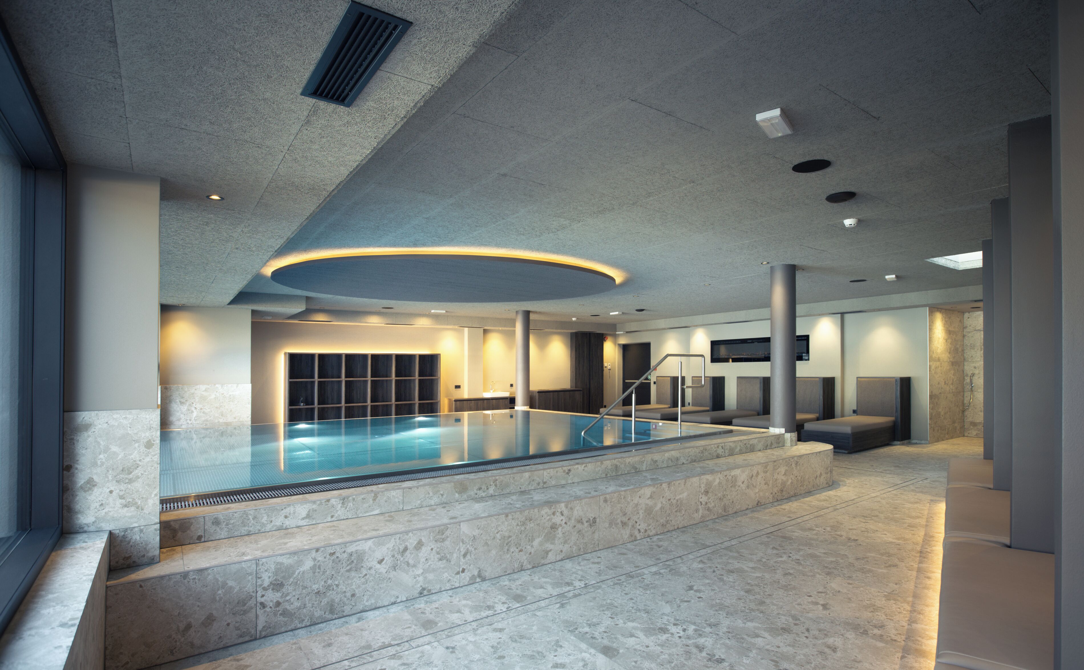Una piscina interior moderna con barrera de vidrio, escalones de piedra e iluminación empotrada.