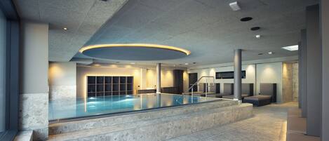 Una piscina interior moderna con barrera de vidrio, escalones de piedra e iluminación empotrada.