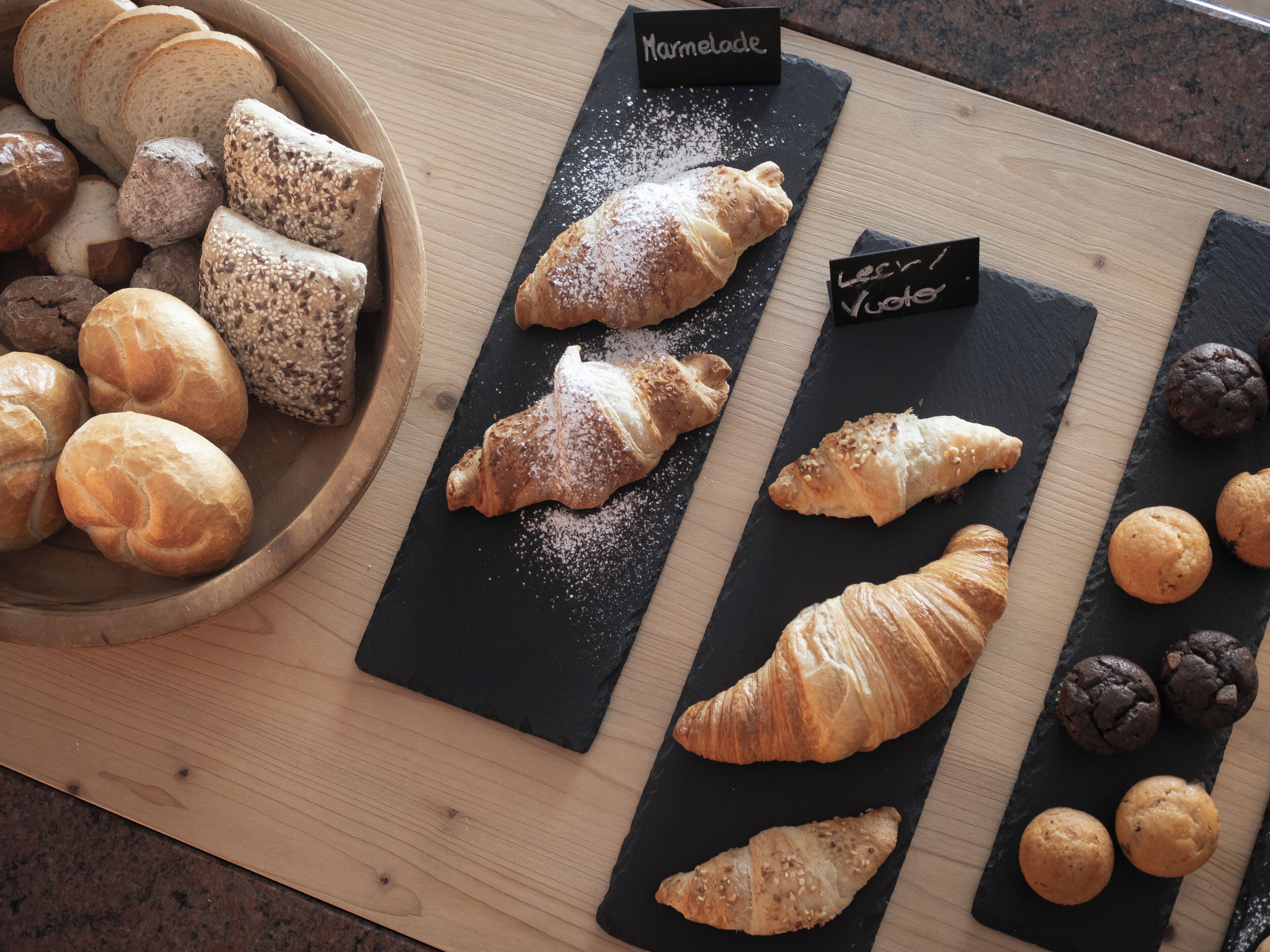 Verschiedene Backwaren wie Brot, Croissants und Kekse auf einer Holz- und einer Schieferplatte.