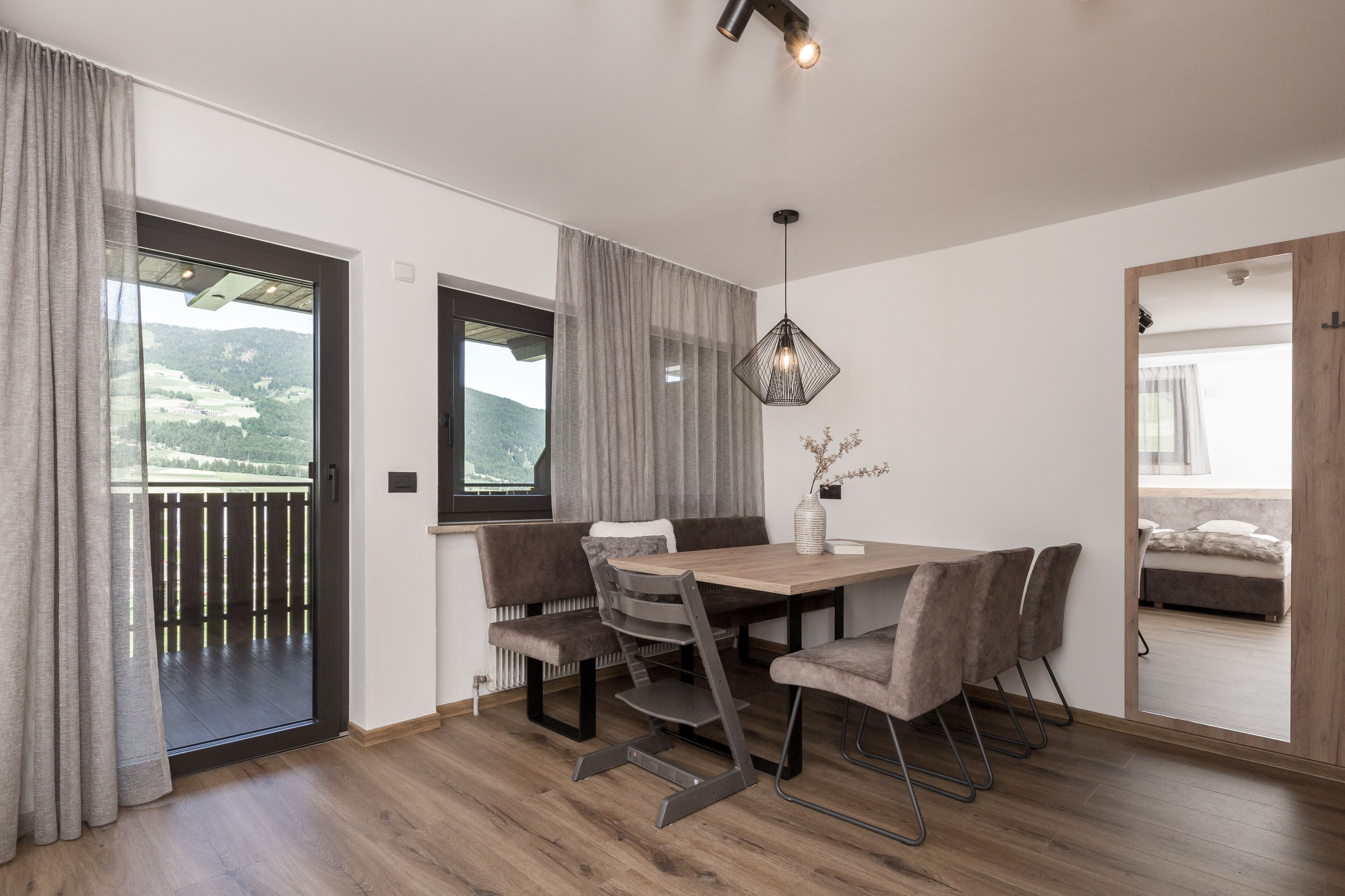 A modern dining area with a wooden table, cushioned chairs, and a pendant light.