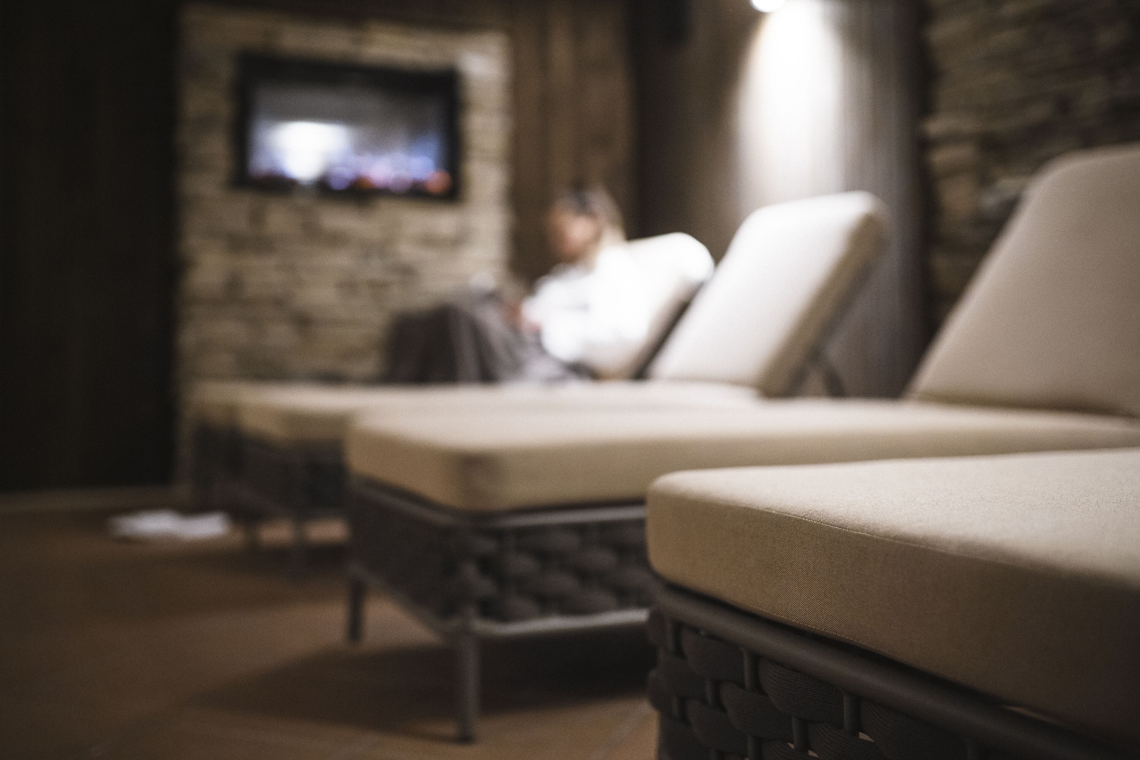 A blurred room with a television mounted on a brick wall, a sofa, and a chair.