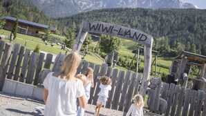 Ein Holzschild mit der Aufschrift 'WIWI-LAND', umgeben von einem Holzzaun, mit Bergen im Hintergrund.