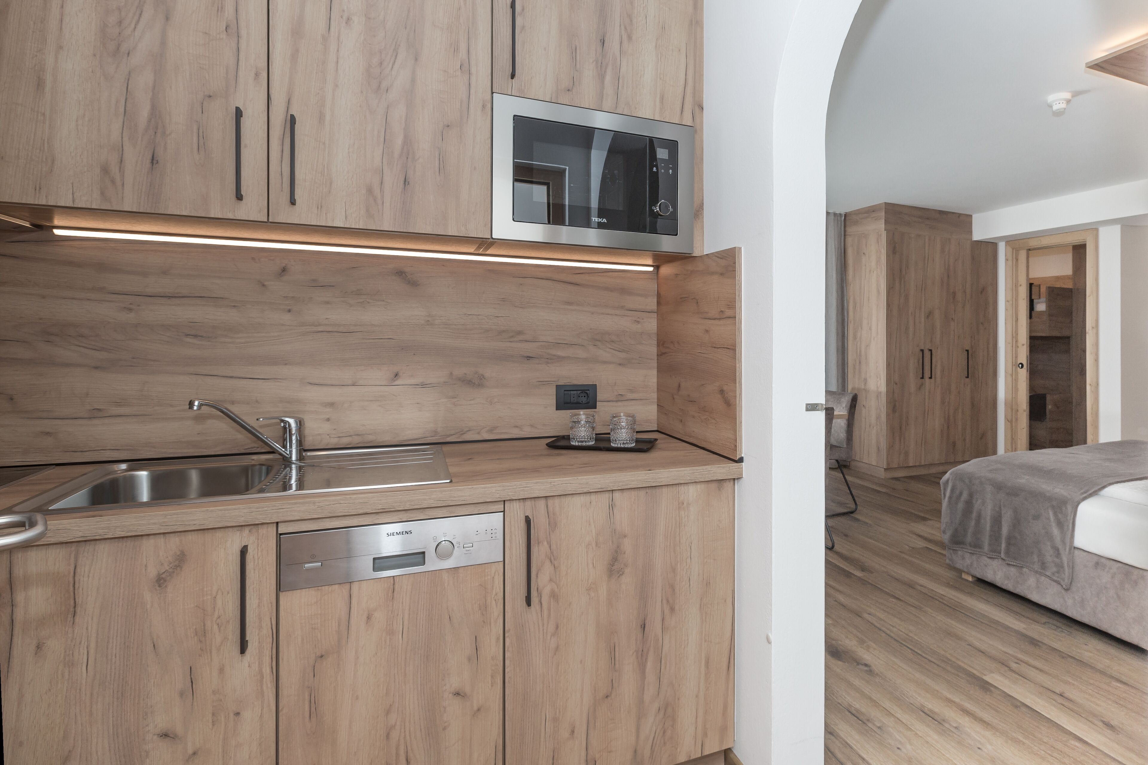 A modern kitchen with wooden cabinets, a built-in microwave, a Siemens dishwasher, and a stainless steel sink.