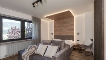 Een moderne slaapkamer met een groot raam, een bank, een bed en een nachtkastje.