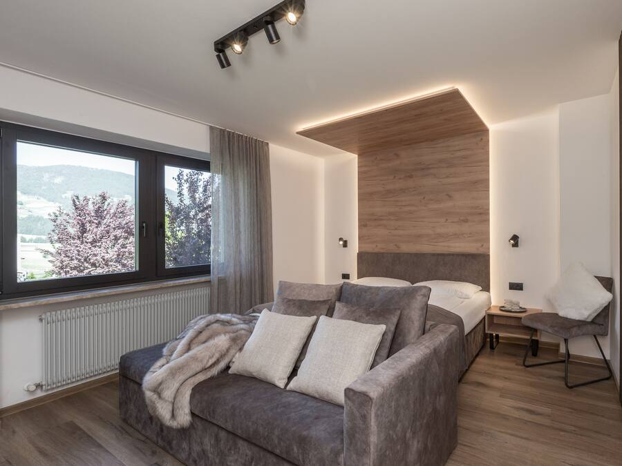 Een moderne slaapkamer met een groot raam, een bank, een bed en een nachtkastje.