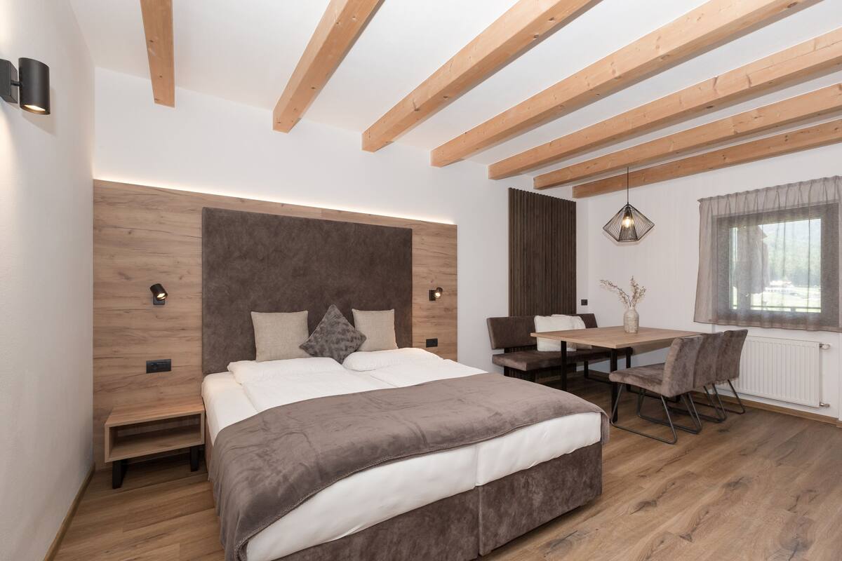 A modern bedroom with a large bed, wooden beams, a desk, and a window.
