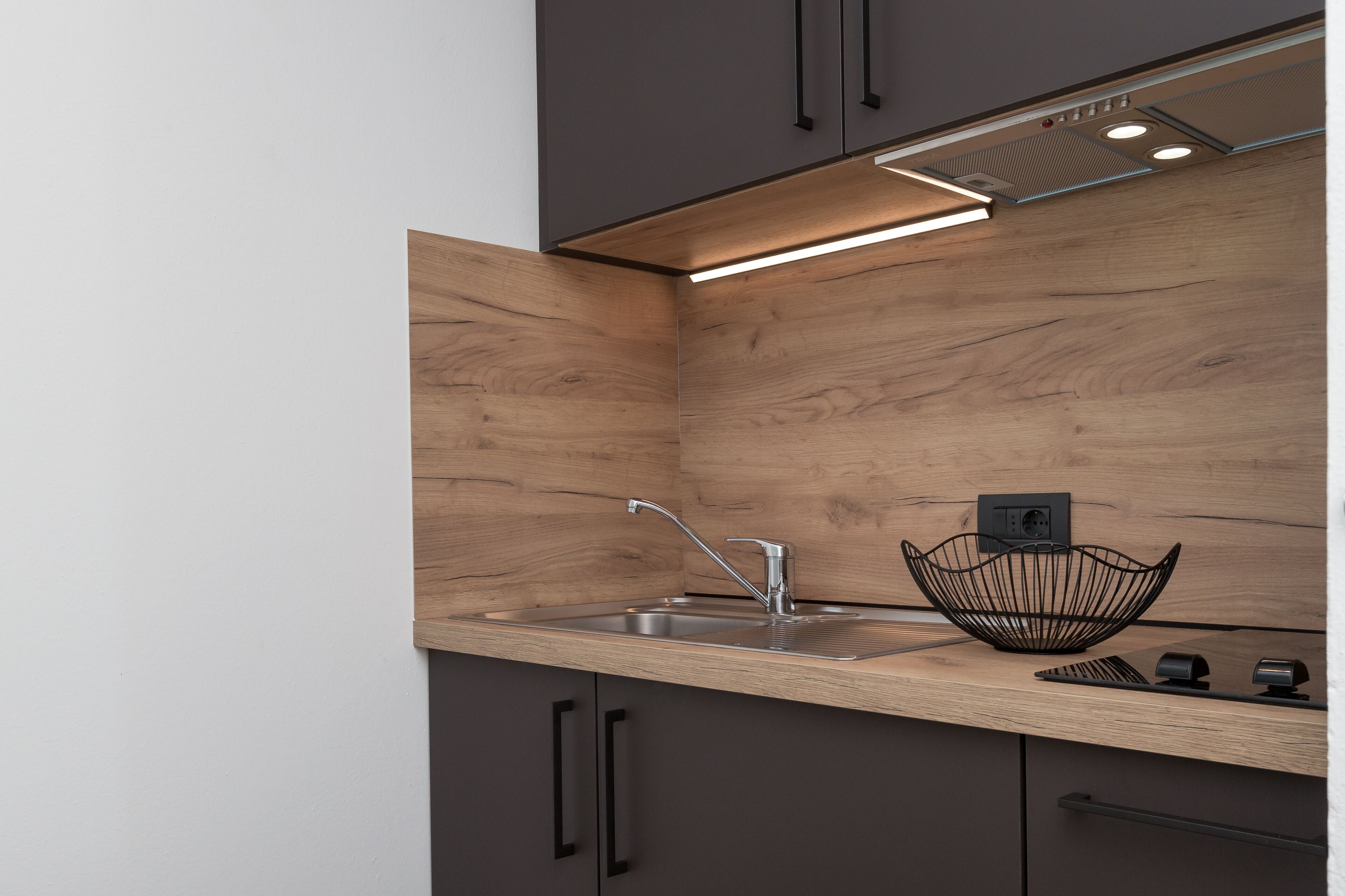 Une cuisine moderne dotée d’un plan de travail en bois, d’un évier en acier inoxydable et de poignées noires sur les placards.