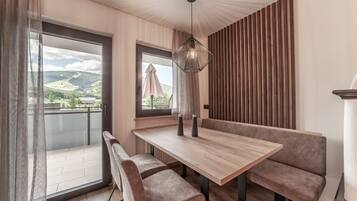 A modern dining area with a wooden table and cushioned benches, a hanging light fixture, and a view of a balcony with a glass door.