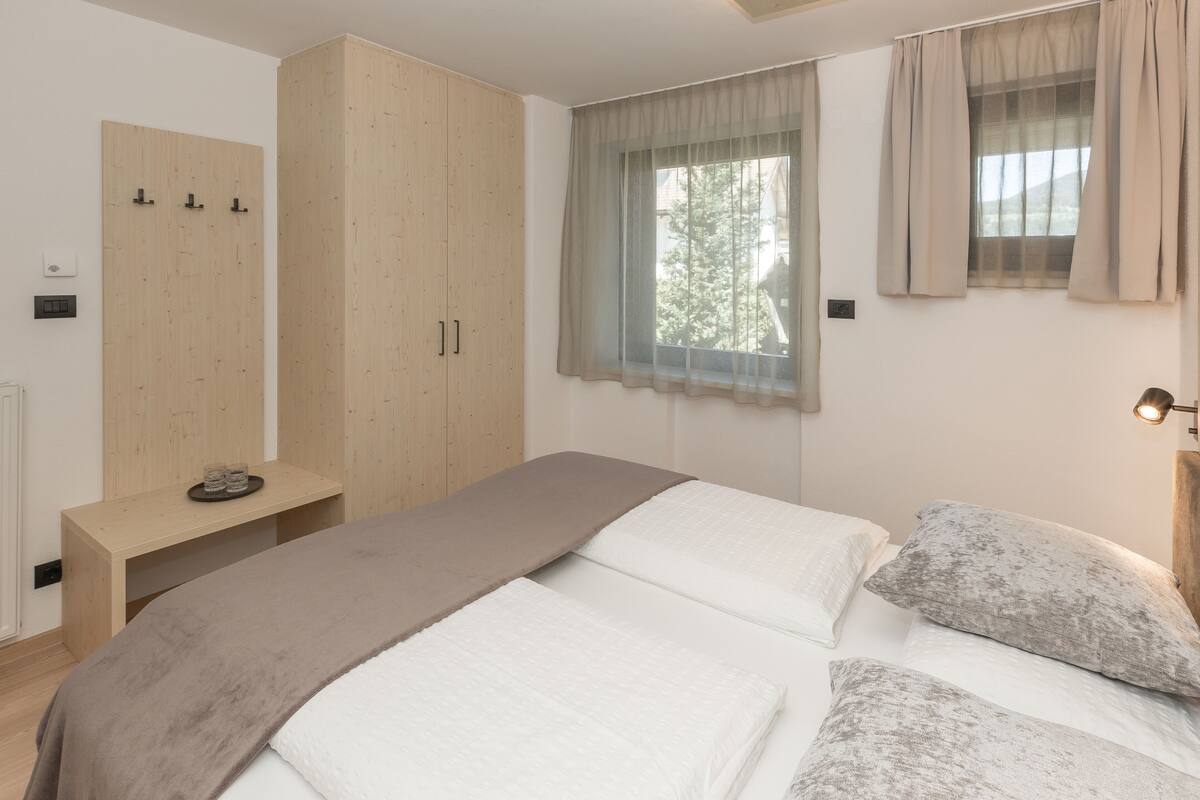 A bedroom with a bed, a wooden wardrobe, a bedside table, and a window with curtains.