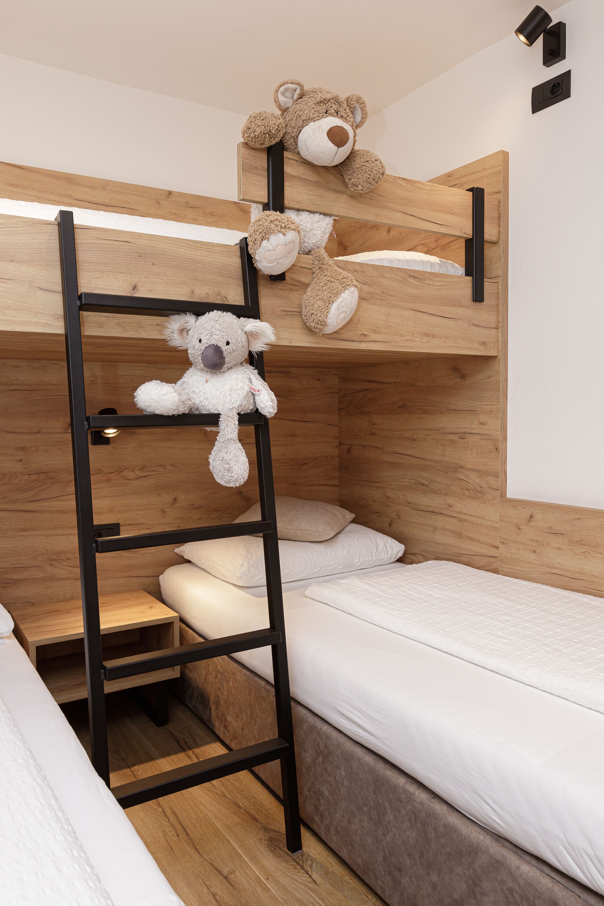 Una cama litera con dos osos de peluche, una mesita de noche y una lámpara de pared.