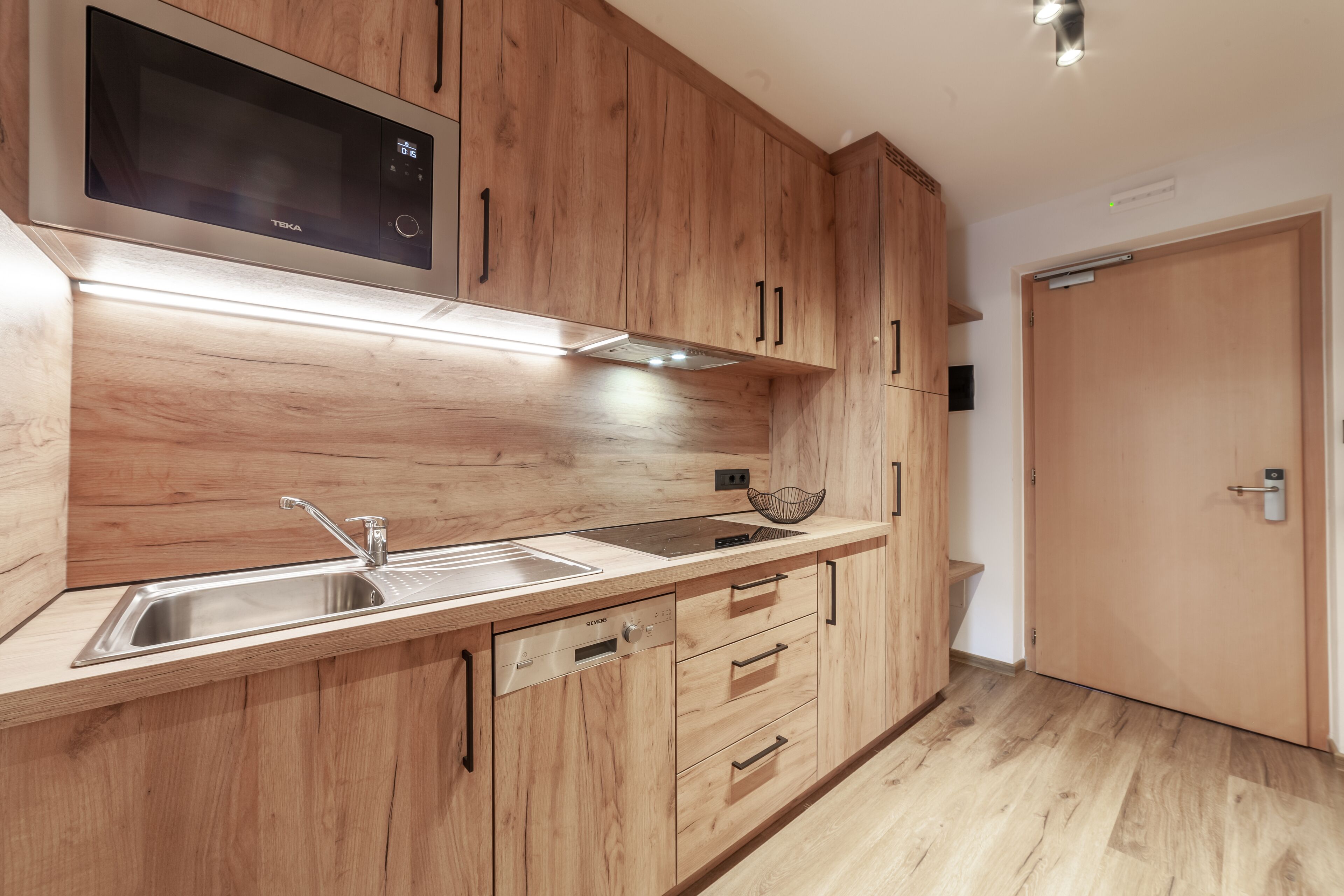 A modern kitchen with wooden cabinets, stainless steel appliances, and a built-in microwave.
