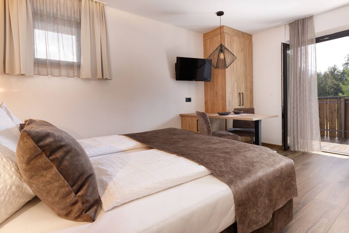 A bedroom with a bed, a desk, a TV, and a balcony.