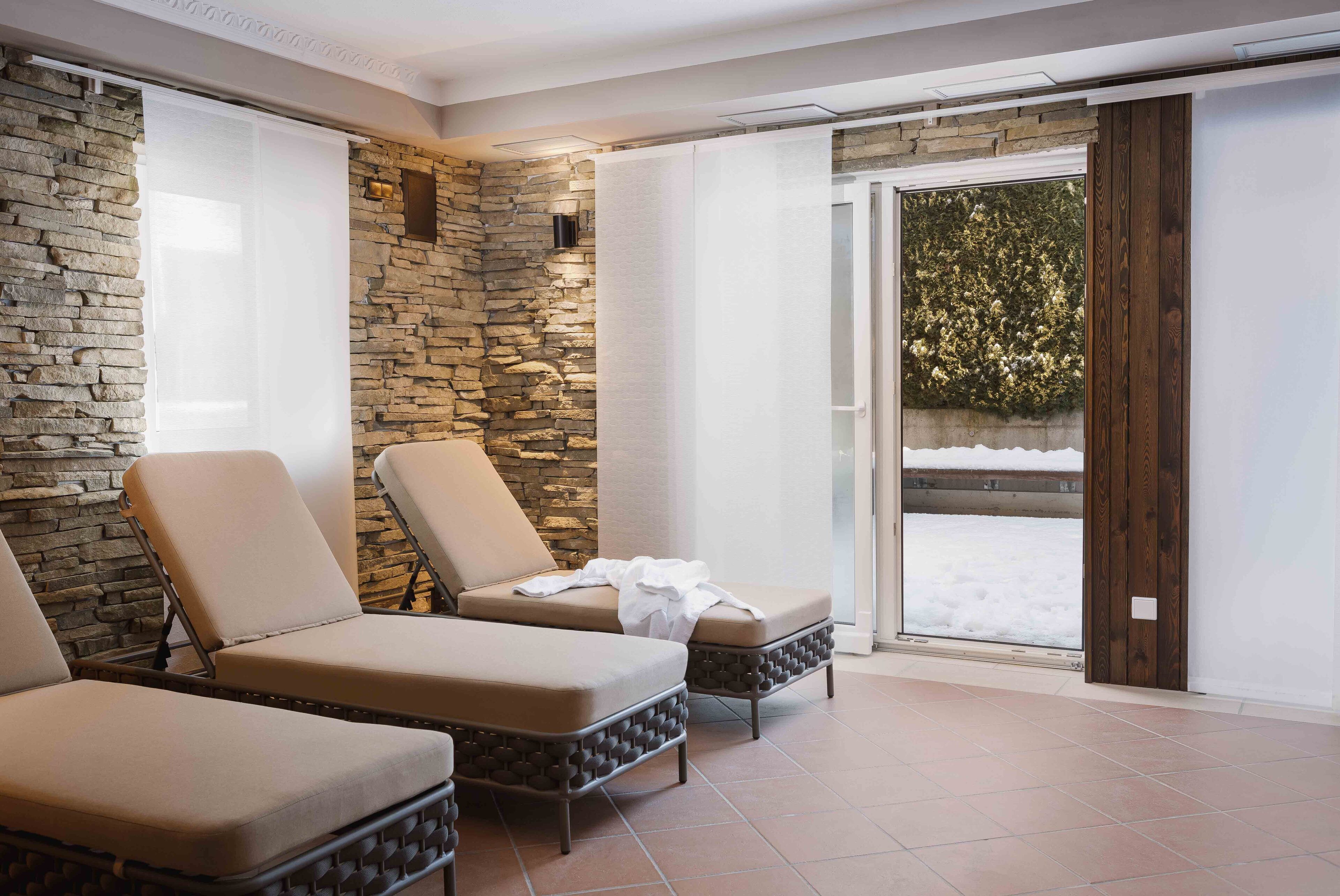 A sunroom with stone walls, two lounge chairs, and a sliding glass door leading to a snowy outdoor area.