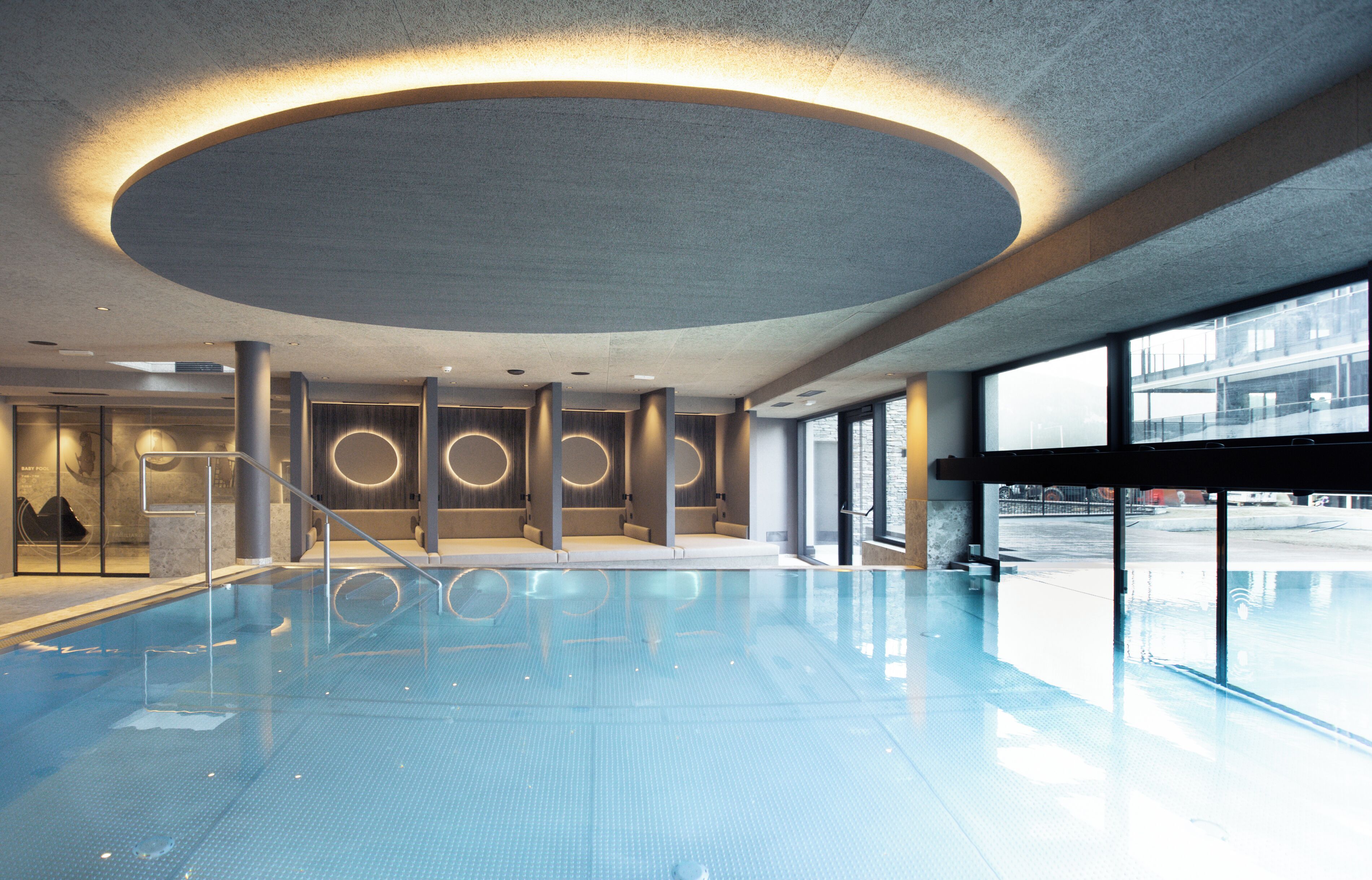 An indoor swimming pool with a modern design, featuring a large circular ceiling and large windows.