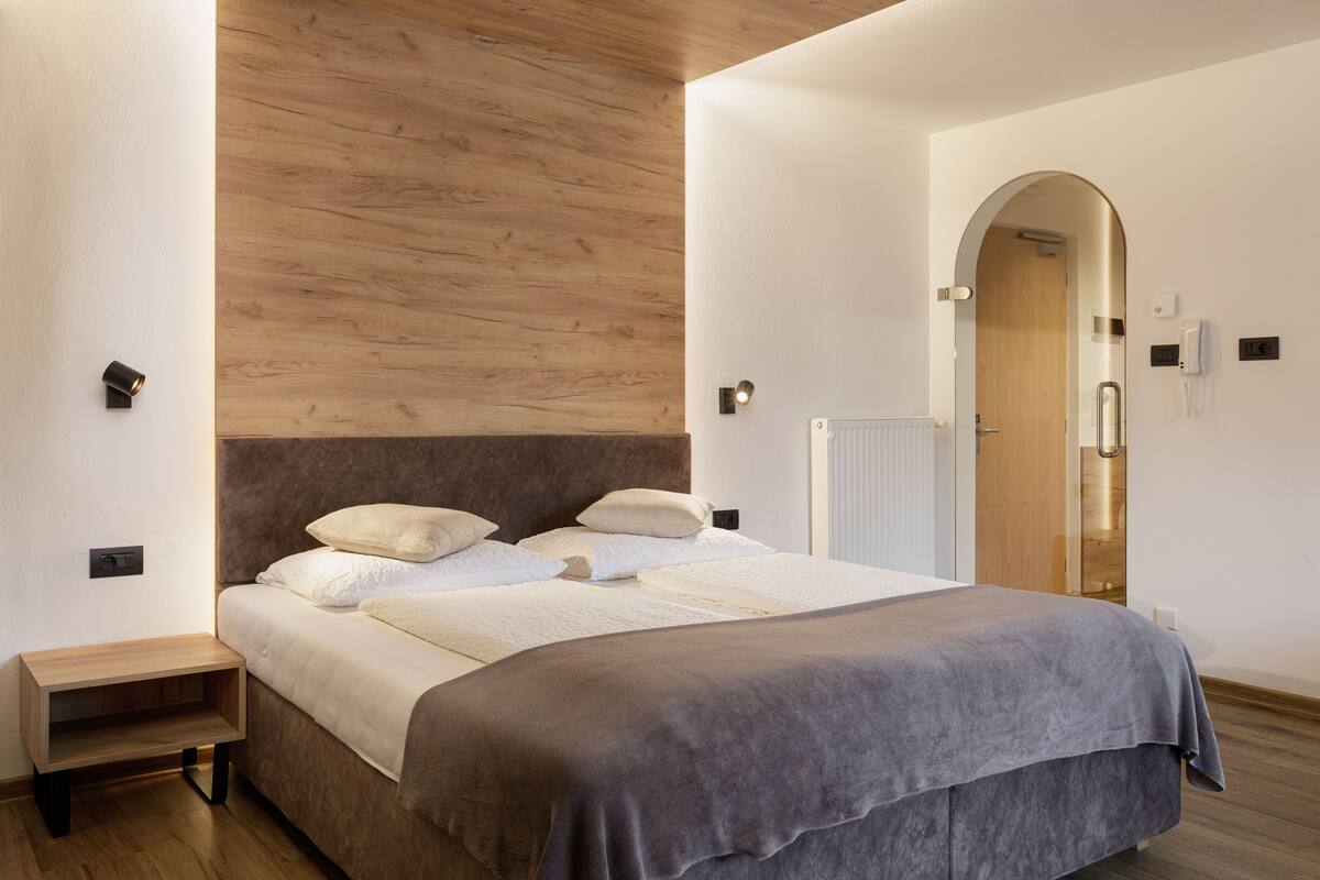 A modern bedroom with a wooden headboard, a bedside table, a radiator, and a door with a glass panel.
