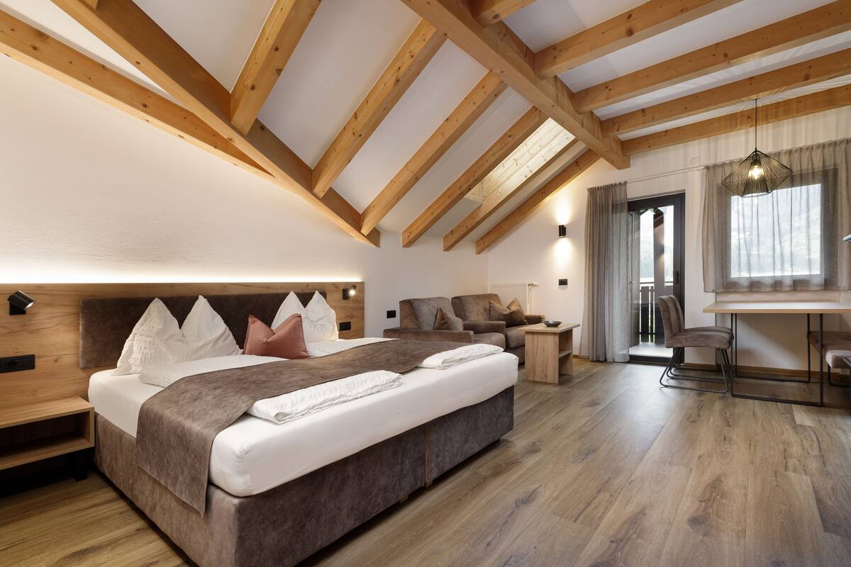 A bedroom with a large bed, wooden beams, a desk, and a chair.