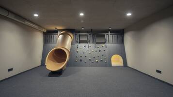 Um quarto com um escorregador cilíndrico grande, paredes acolchoadas e uma parede de escalada com diversos apoios.