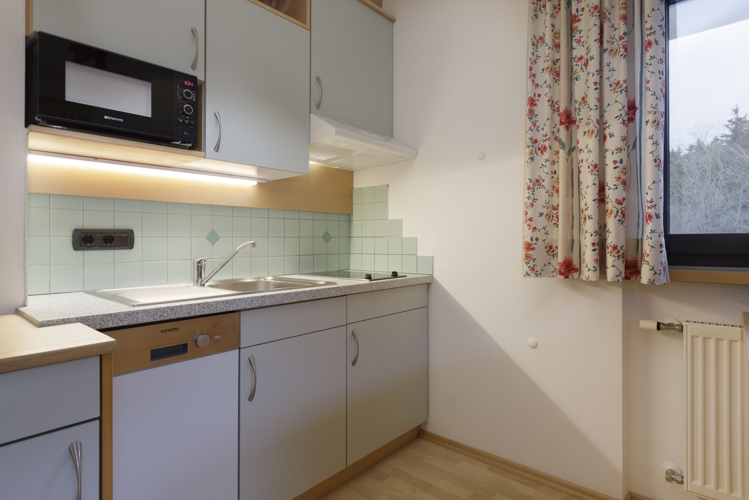 Una cocina con microondas, lavaplatos doble y armarios de tonos claros.