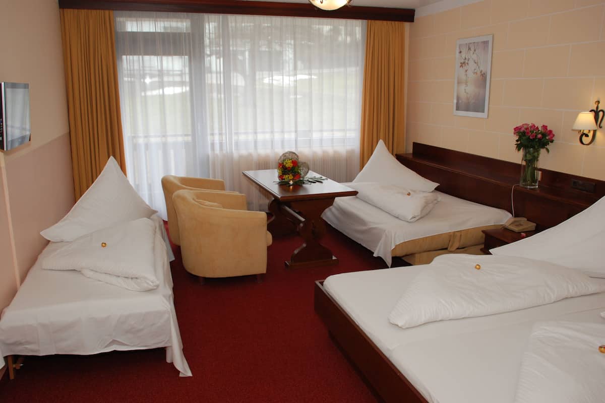 A hotel room with two single beds, a double bed, a desk with a chair, a small table with a vase of flowers, and a television on the wall.