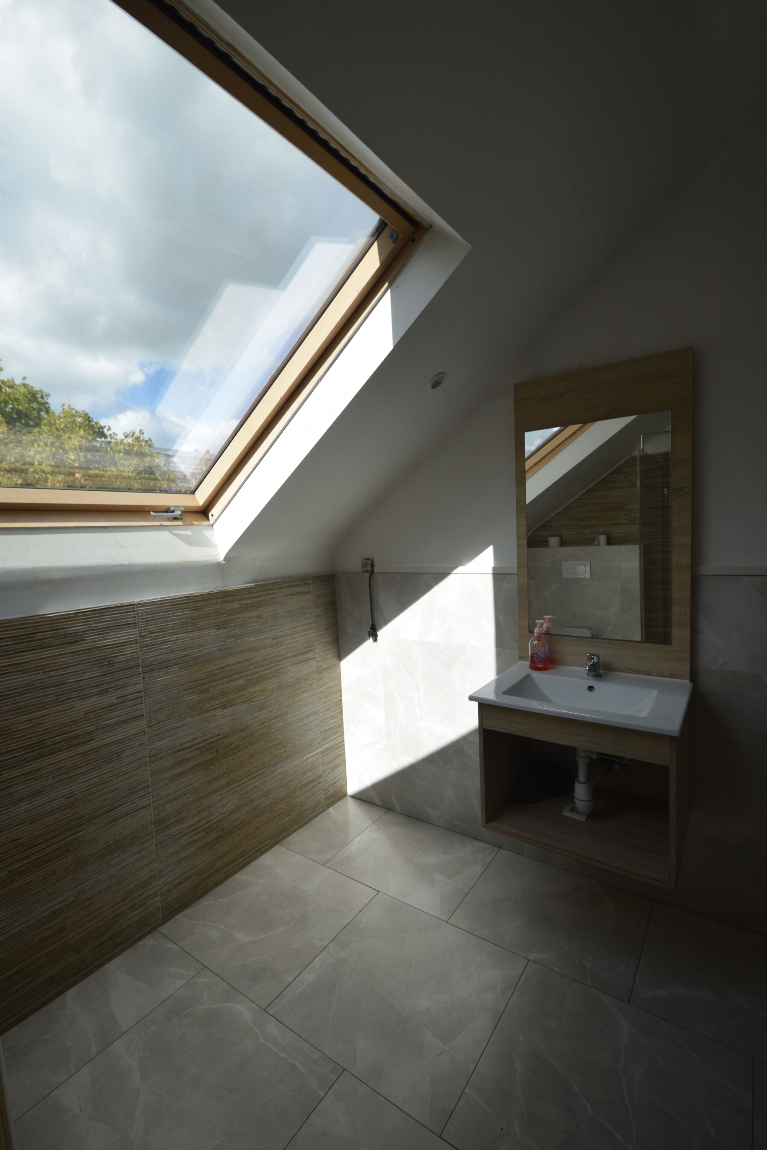 Une lucarne dans une salle de bain avec un meuble-lavabo en bois et un miroir.