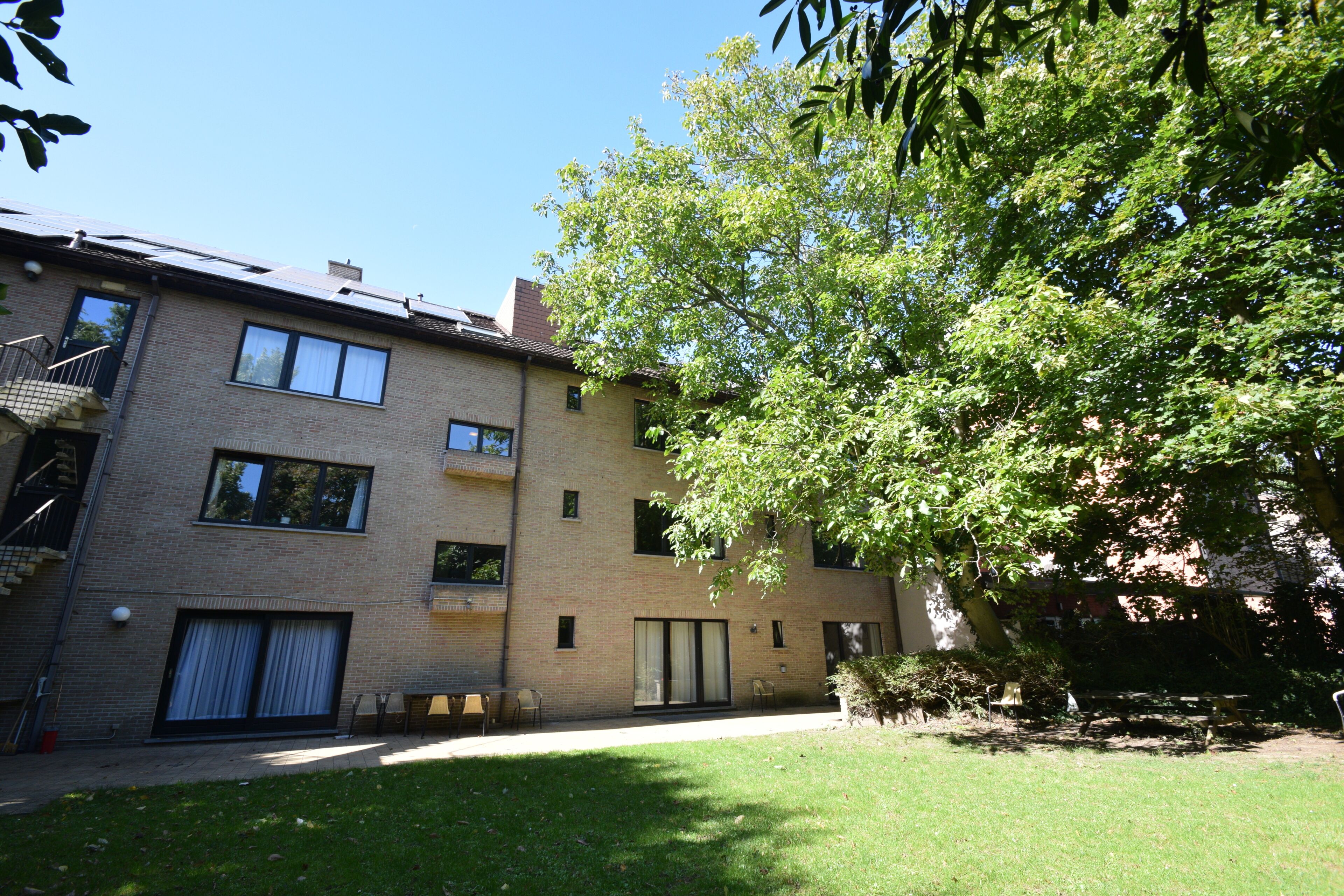A multi-story building with a grassy yard, a tree, and a clear blue sky.