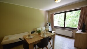 A room with a bed, a dining table with chairs, a small kitchenette, and a window with curtains. - Budget Flats Brussels (Brussels)