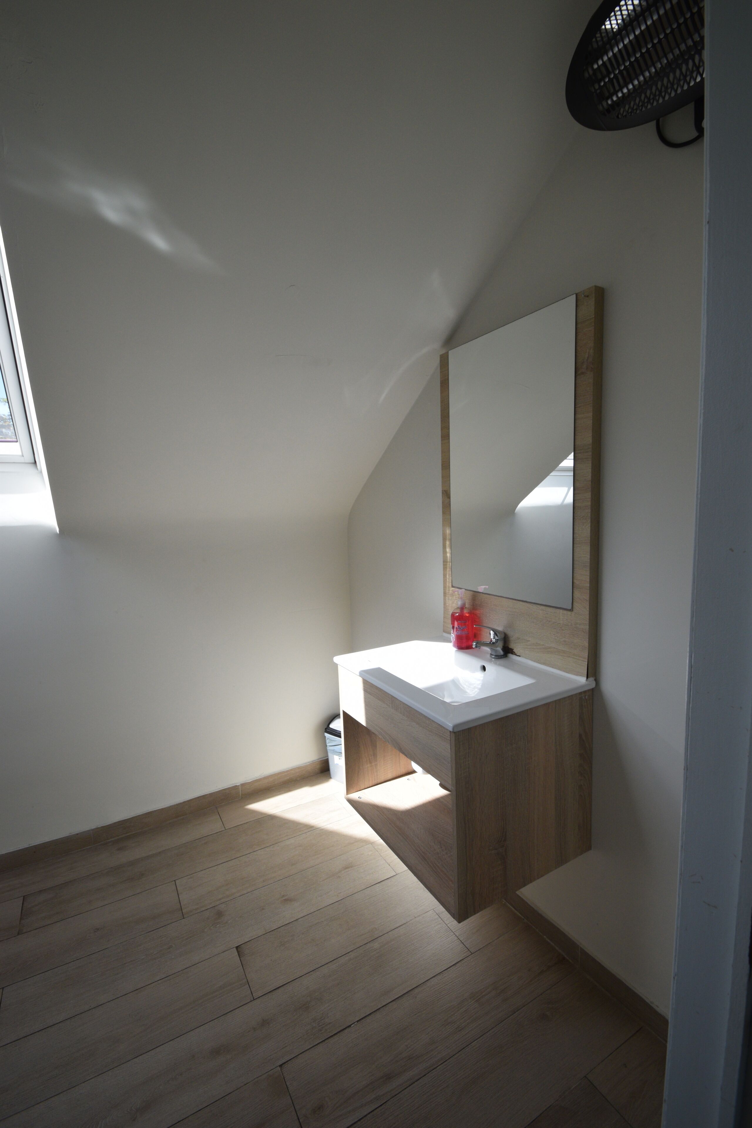 A small, modern bathroom with a wooden vanity, a white sink, and a large mirror.