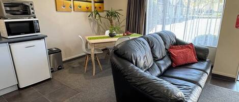A compact living space with a kitchenette, a dining area, and a seating area with a leather sofa and a red pillow.