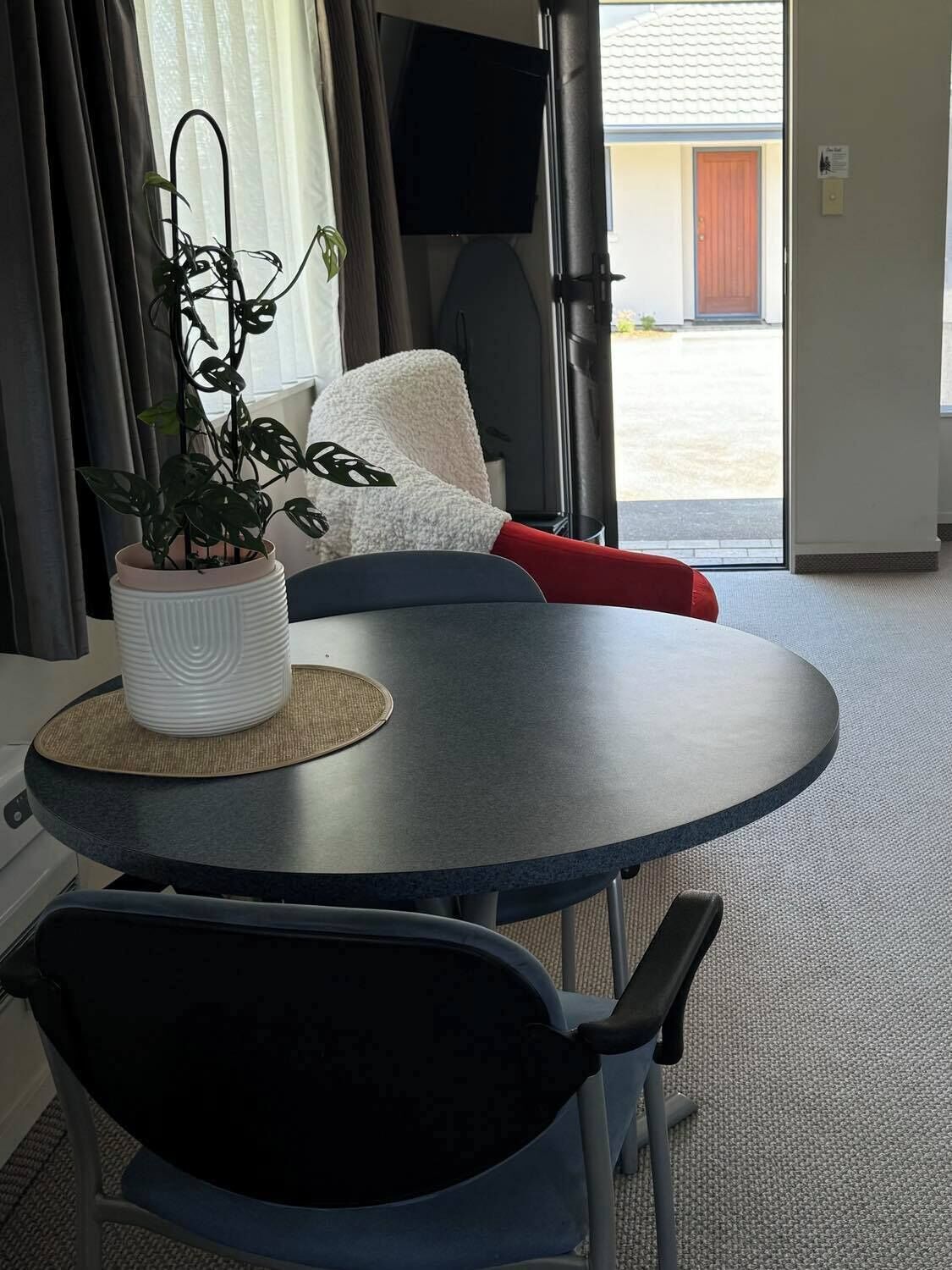 A small round table with a potted plant, a cushion, and a red item on it.