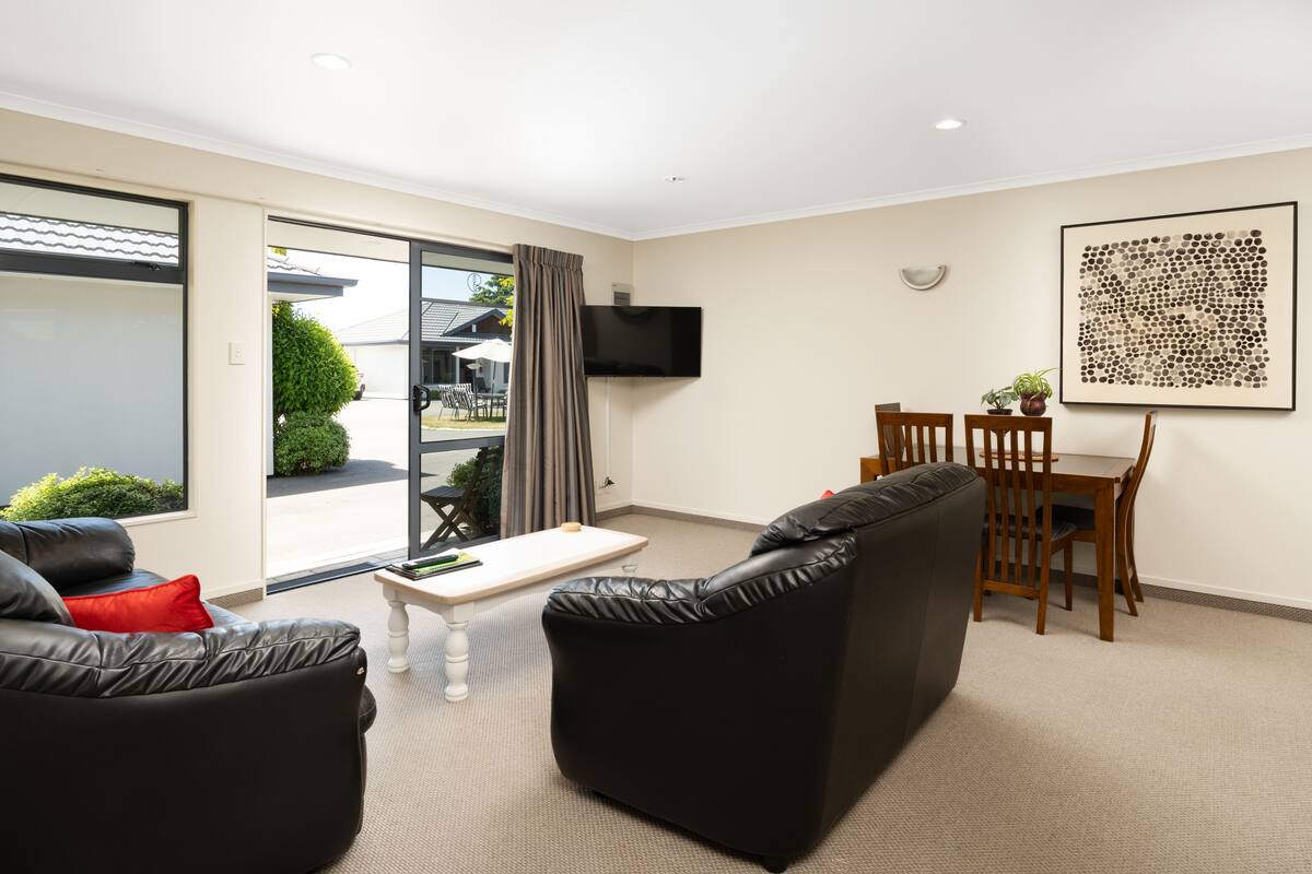 A modern living room with a sofa, a coffee table, and a dining area with chairs and a TV mounted on the wall.