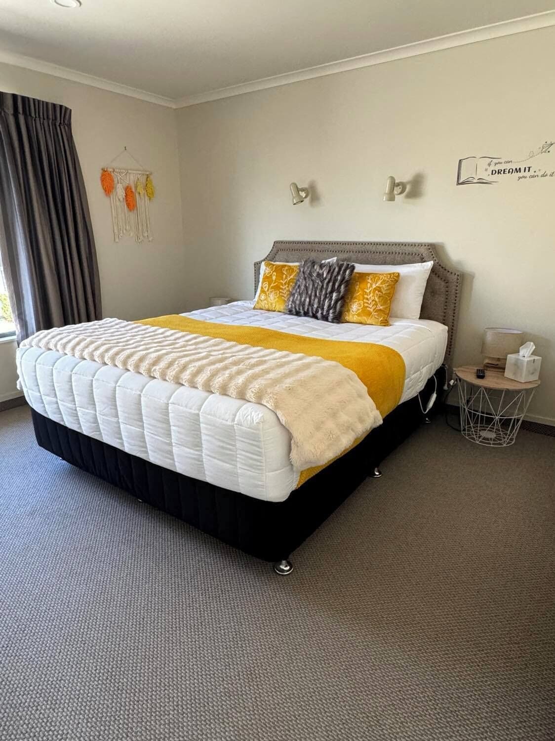 A neatly made bed with a white and yellow bedspread, a grey headboard, and decorative pillows.