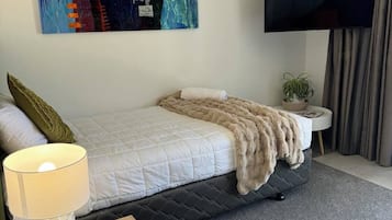 Habitación de hotel con cama, televisión, un cuadro y una mesa con lámpara y control remoto.