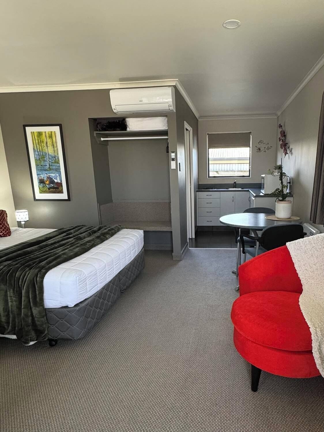 A compact hotel room with a bunk bed, a small kitchenette, a dining table, and a red armchair.