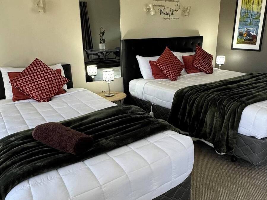 A hotel room with two beds, each with white bedding and red patterned pillows. There is a black headboard on one bed and a mirror above the bed. A motivational quote is displayed on the wall.
