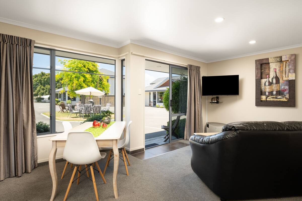 A modern living room with a dining area, large windows, a flat-screen TV, and a painting on the wall.