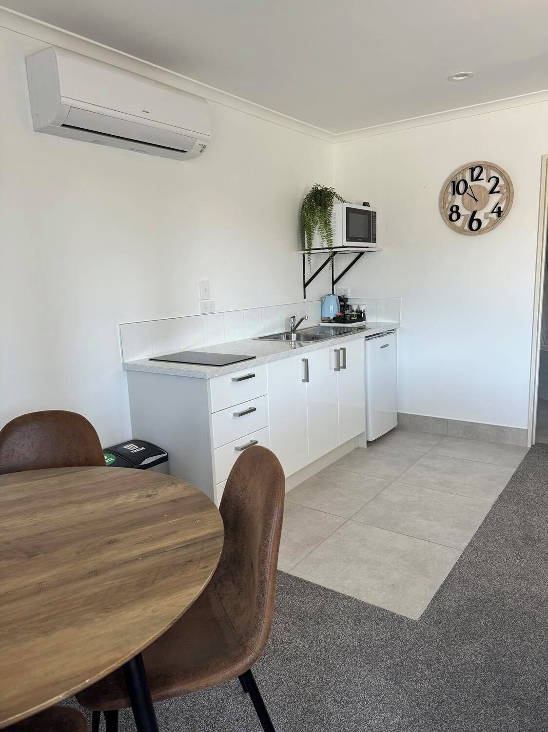 A modern kitchen with white cabinets, a microwave, and a clock on the wall.