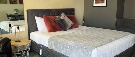 Un dormitorio con una cama grande, una mesita de noche, una silla, una pequeña mesa redonda y una pared con una cita motivacional.
