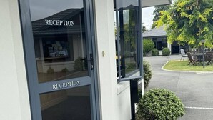 En reception med glasdør, et lille udendørs opholdsområde med bord og stole, samt en velholdt græsplæne.