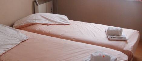A hotel room with two beds, each with white linens and towels. There is a window with red curtains and a wall-mounted air conditioning unit.