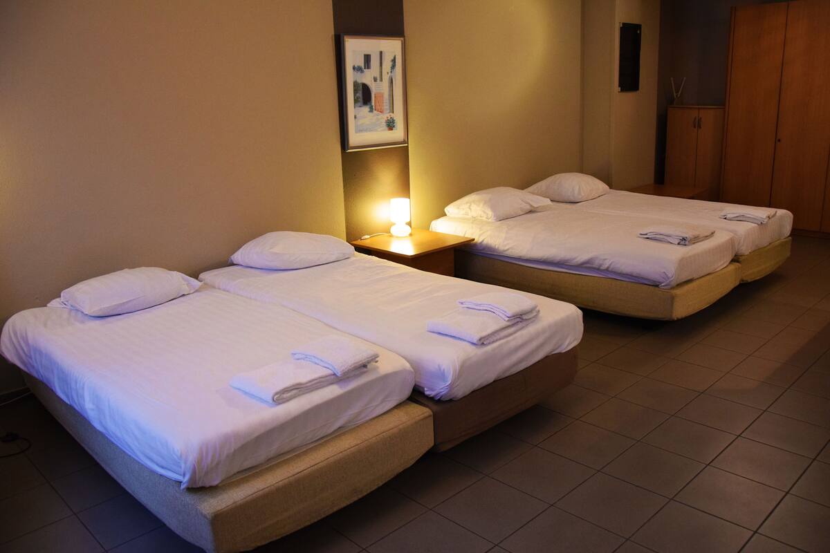 Two single beds with white linens and pillows, a nightstand with a lamp, and a wooden wardrobe in a hotel room.