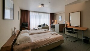 A hotel room with two beds, a desk, a chair, a TV, a desk lamp, and a window with curtains. - City Apartments Antwerp (Antwerp)