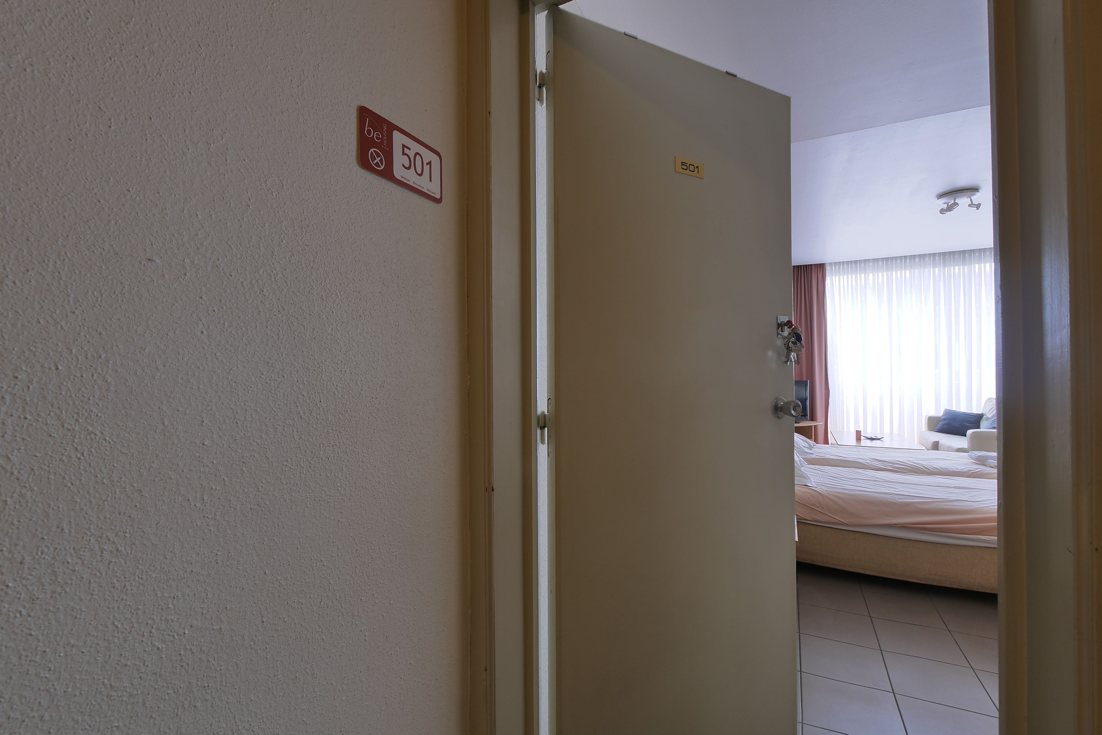 A hotel room with a bed, a nightstand, and a window with curtains.